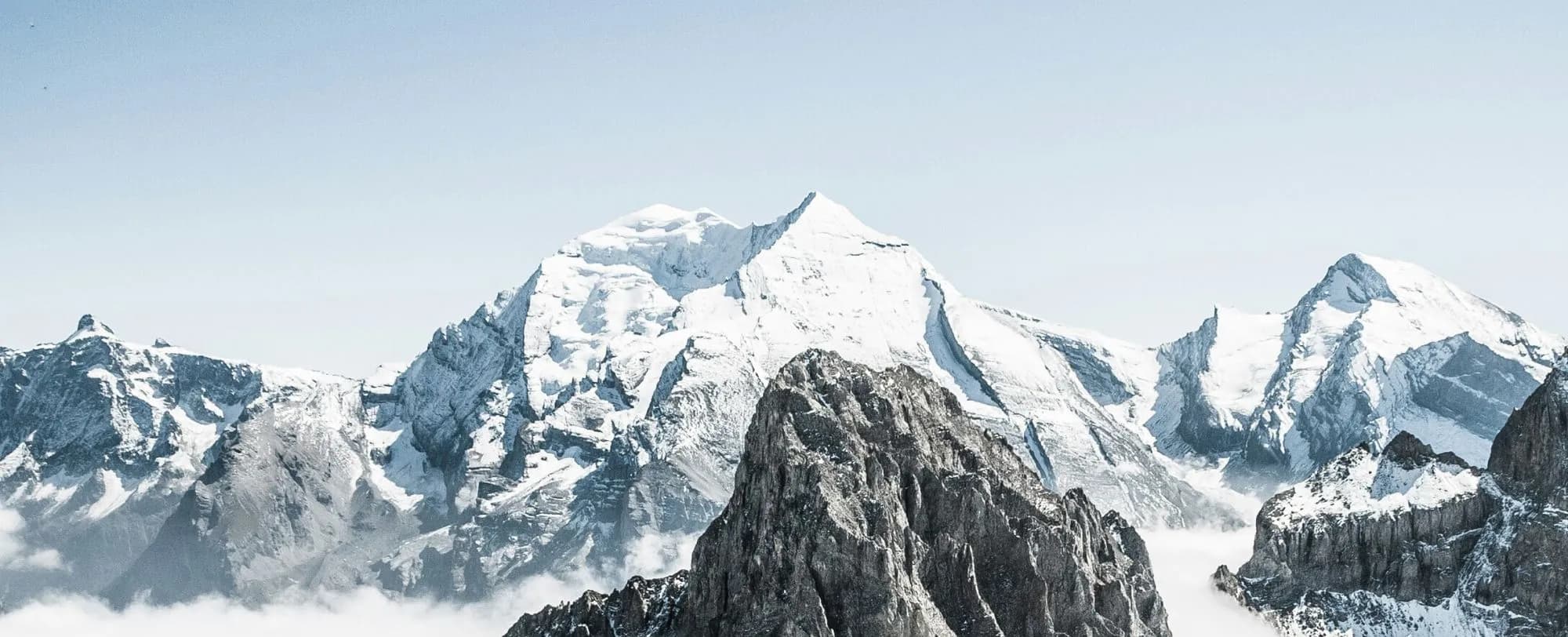 Snow-covered Alpine peaks rising above clouds in a clear winter sky