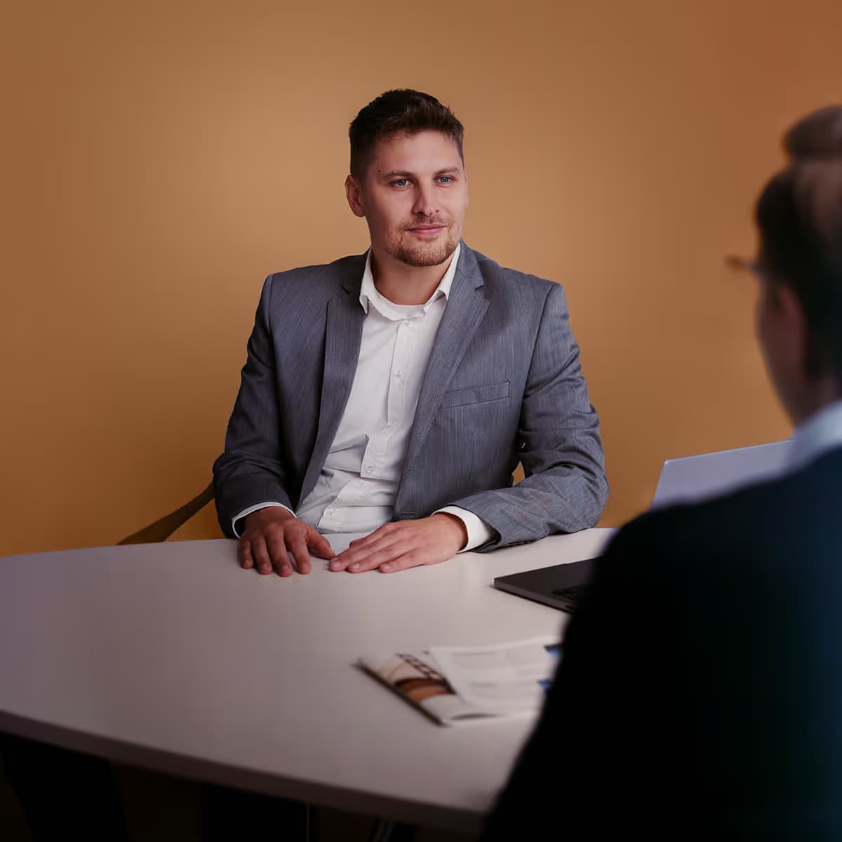 Businessman in a grey suit sitting at a desk during a conversation