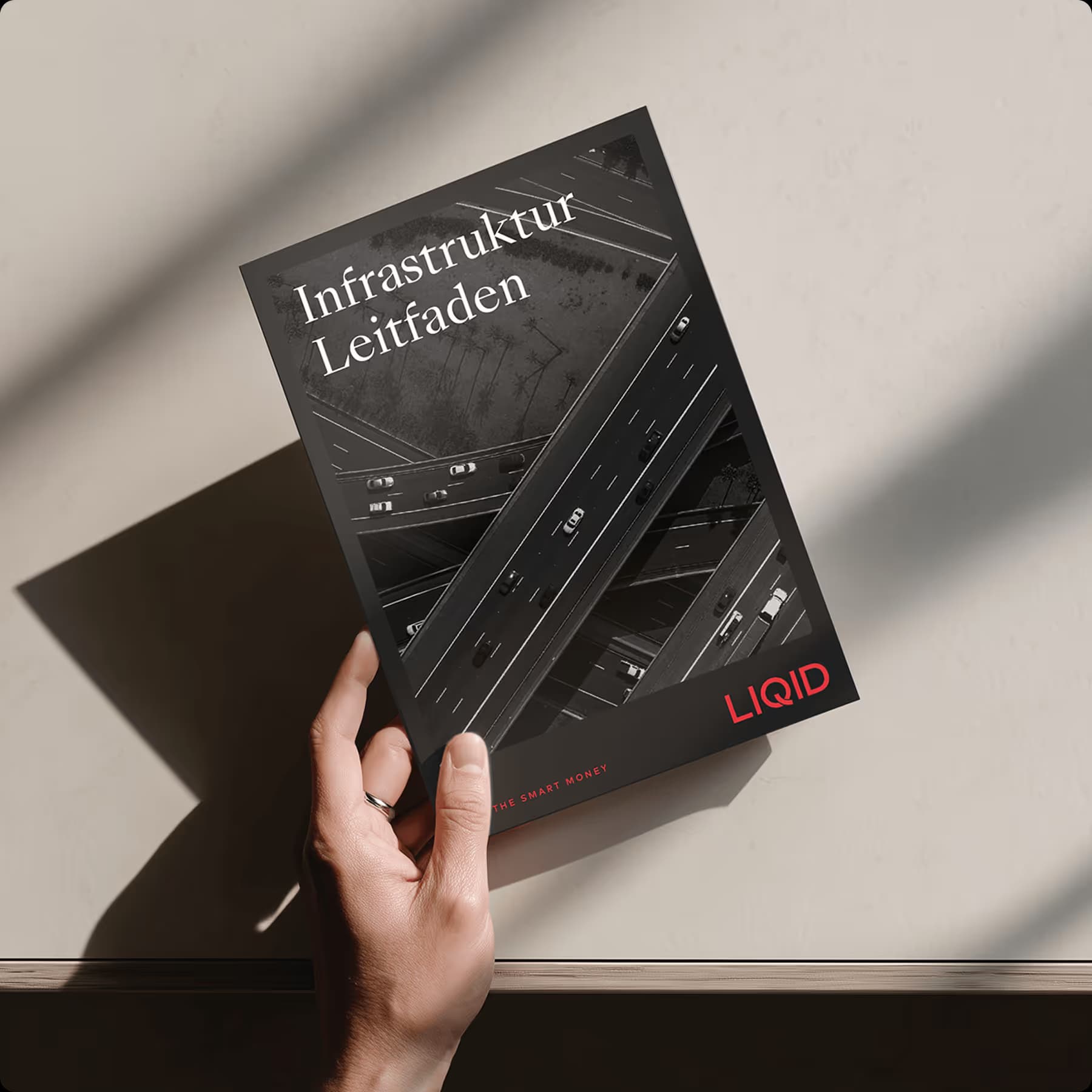 Hand holding the ZUWAX infrastructure guide with a road scene on the cover
