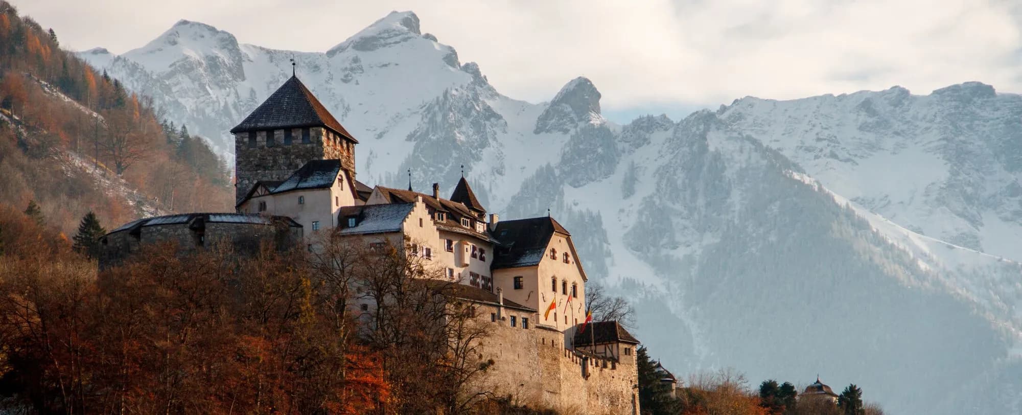 Historic castle on a rock with snow-covered Alps in the background