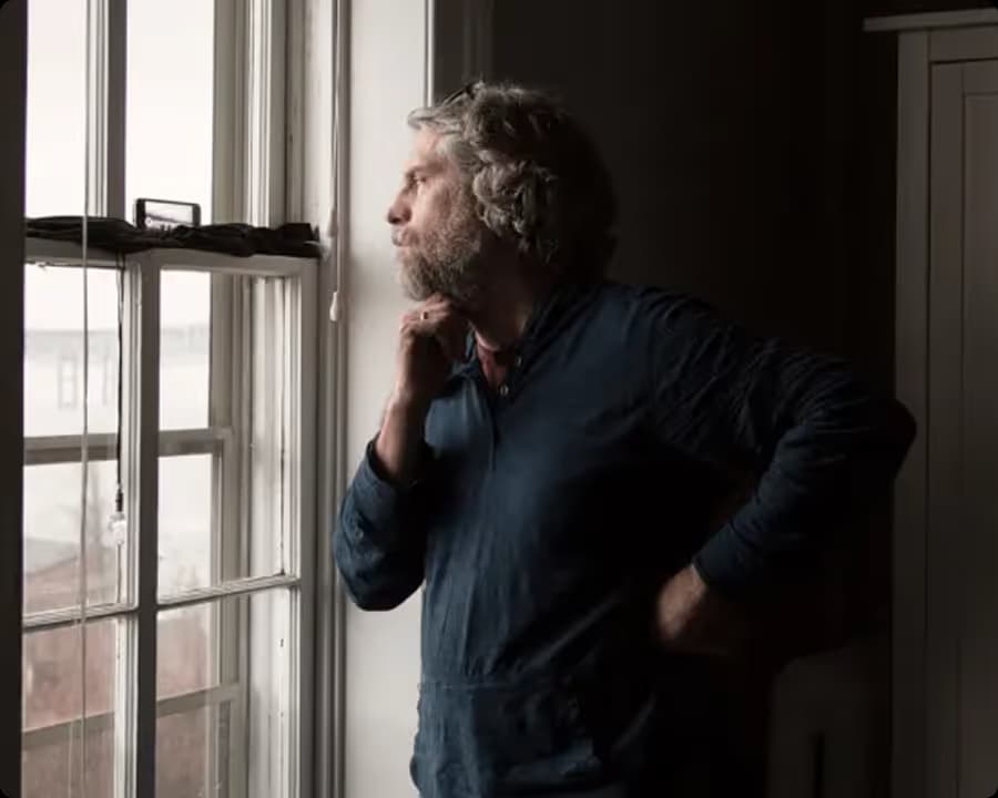 Pensive man looking out of a window, wrapped in daylight