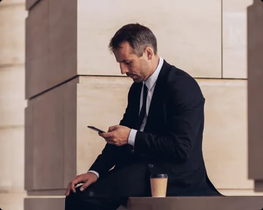 Businessman in a black suit looking at his smartphone with a coffee